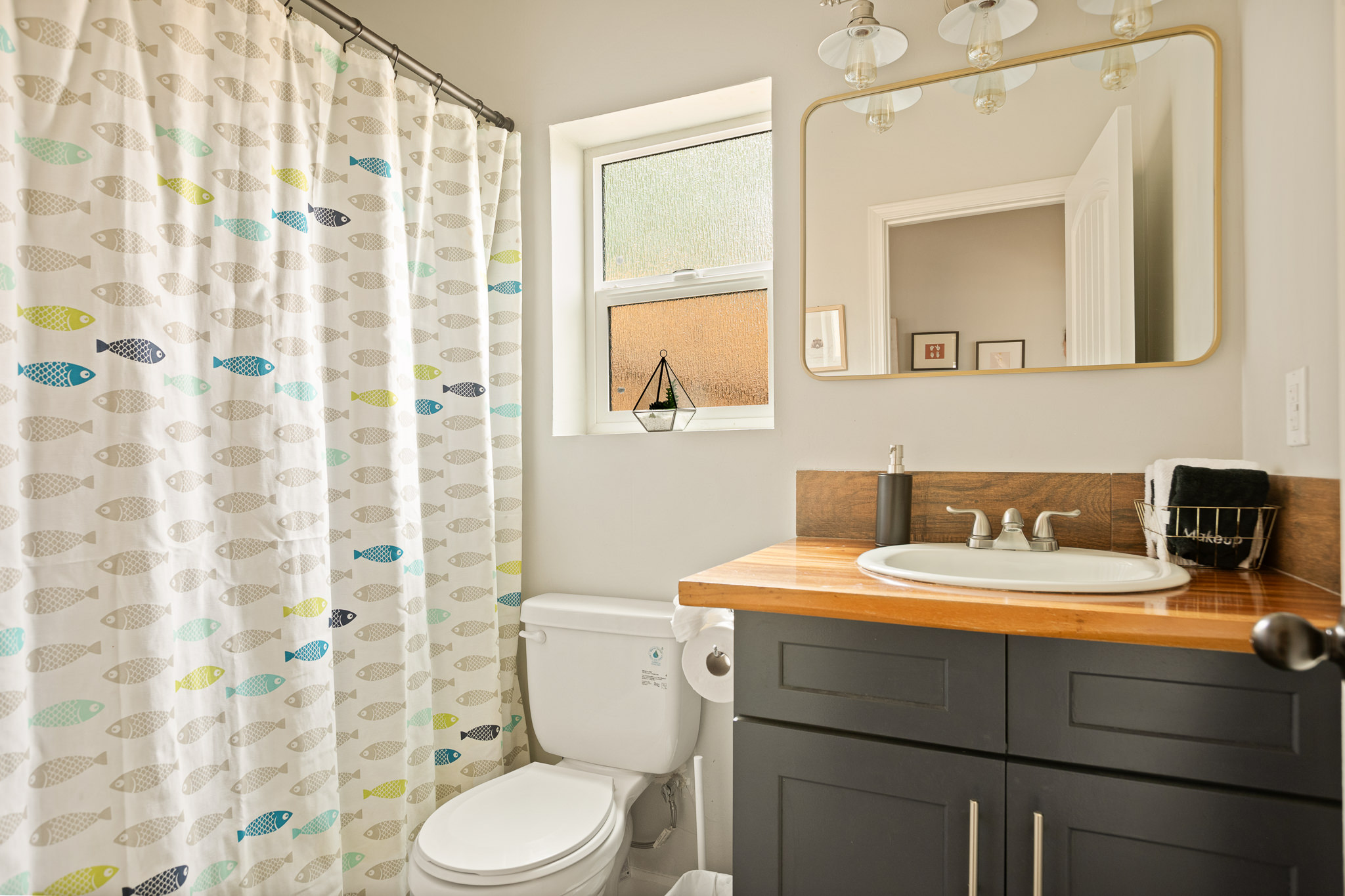 Fish-print shower curtain and wood vanity in the bright second bathroom